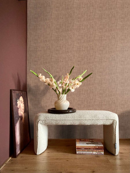 Wohnraum mit strukturierter Tapete in Leinenoptik, gepolsterter Sitzbank, Blumen in Vase und einem Wandbild auf einem Holzboden.