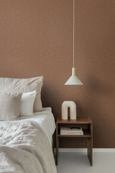 Schlafzimmer mit einer Wand tapeziert mit brauner Vliestapete mit feinem Fischgrätmuster neben einem Nachttisch aus Holz und einem Bett.