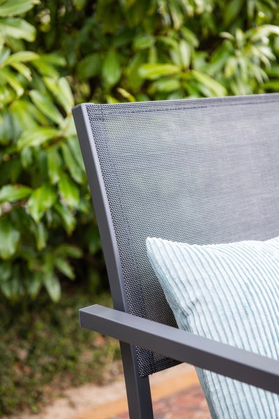 Detailansicht eines Gartenstuhls mit Rückenlehne aus Netzgewebe, Aluminiumgestell und Kissen im Garten.