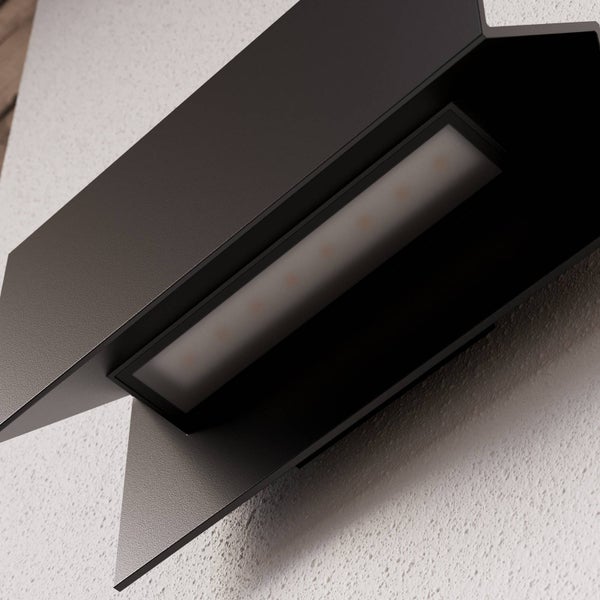 Nahaufnahme einer schwarzen Außenwandleuchte mit integriertem LED-Panel und geometrischem Design an einer Fassade.