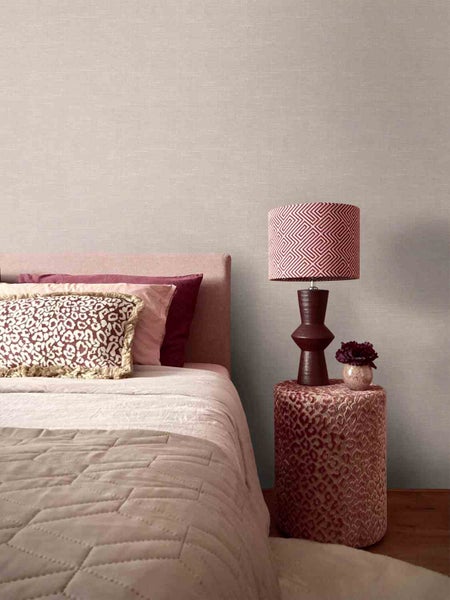 Schlafzimmer mit strukturierter Tapete, gepolstertem Bett, Kissen mit Tiermuster, Hocker und Tischleuchte mit geometrischem Schirm.