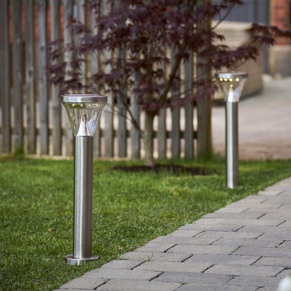 Zwei Solarleuchten aus Metall im Garten entlang eines gepflasterten Weges.