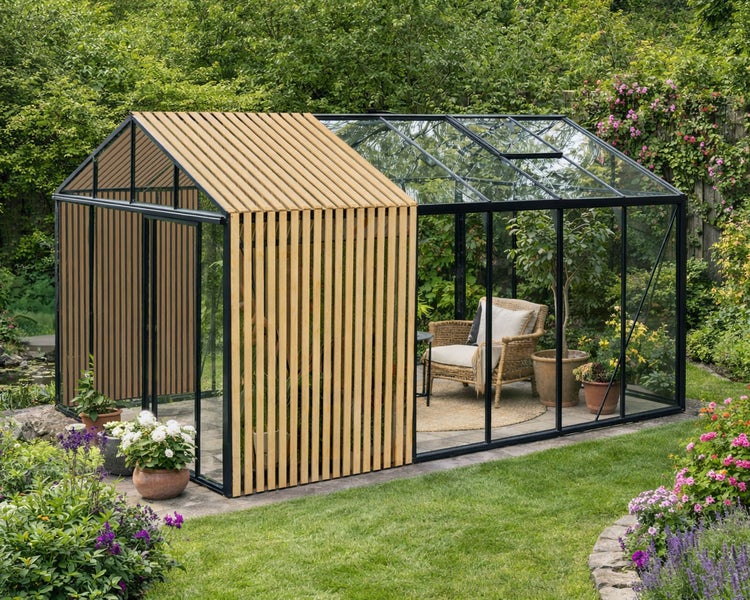 Modernes Gewächshaus mit schwarzem Metallrahmen, Glaselementen und Holzlamellen, eingerichtet mit Sessel in einem üppigen Garten.