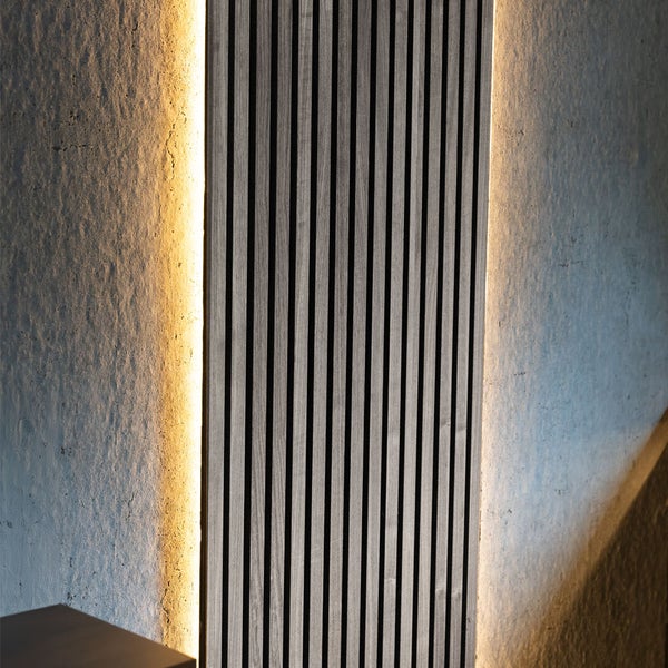 Wandpaneel aus Holzlamellen mit indirekter Hintergrundbeleuchtung auf einer strukturierten Wand.