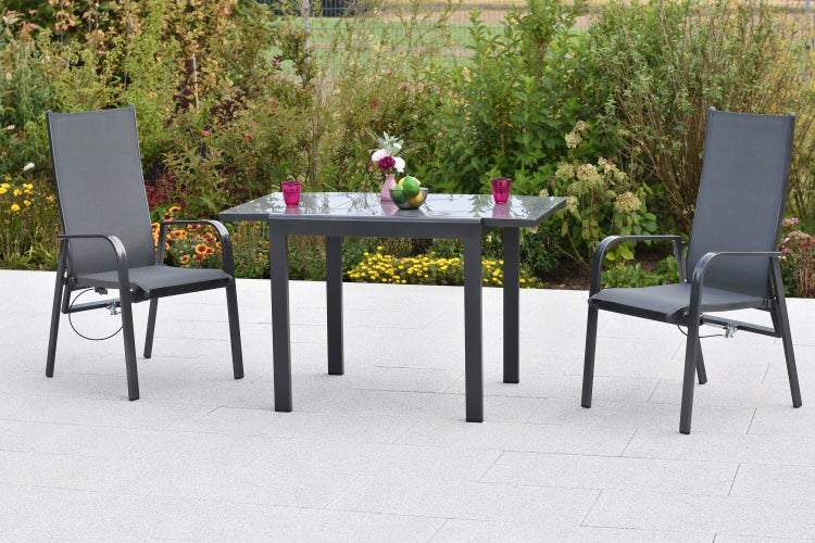 Modernes Gartenmöbel-Set mit einem Metalltisch mit Glasplatte und zwei verstellbaren Hochlehner-Stühlen aus Textilgewebe auf einer Steinterrasse.