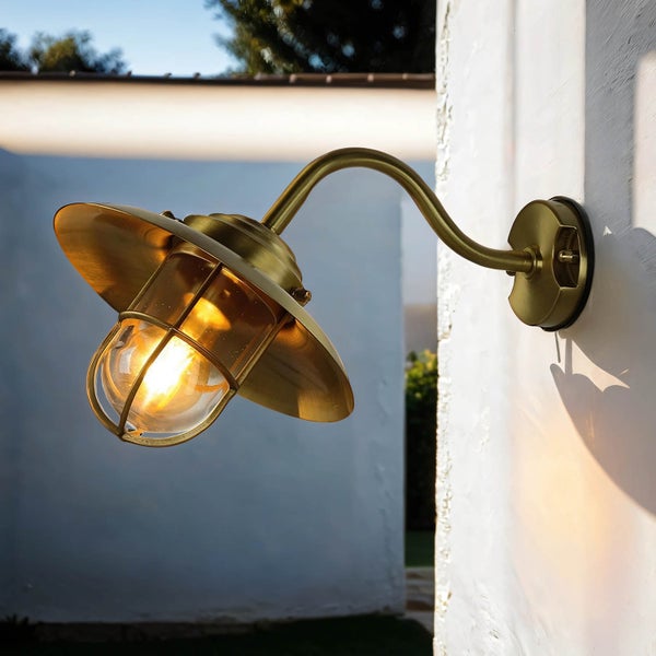 Messingfarbene Wandleuchte mit Schutzkorb an einer Hauswand