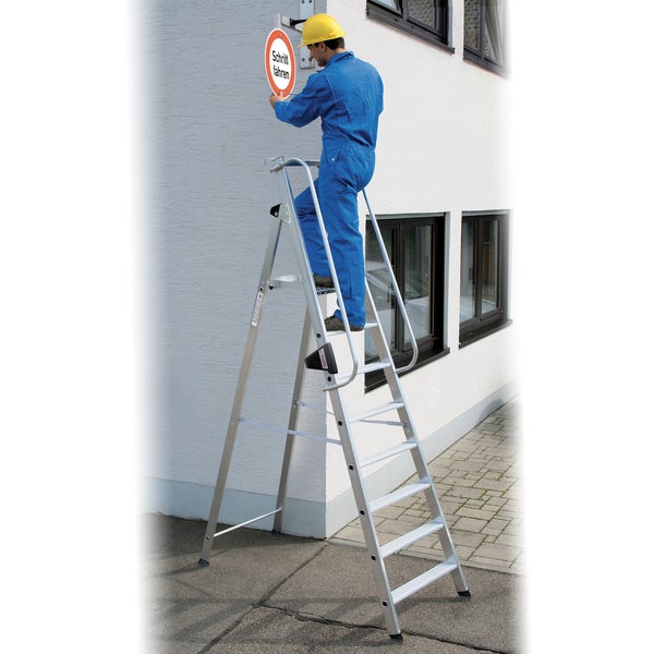 Eine Person auf einer Aluminium-Stufenleiter montiert ein Verkehrsschild an einer Fassade.