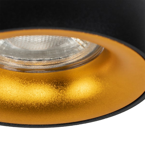 Nahaufnahme eines Strahlers mit schwarzem Gehäuse, goldfarbener Innenseite und sichtbarem Leuchtmittel.