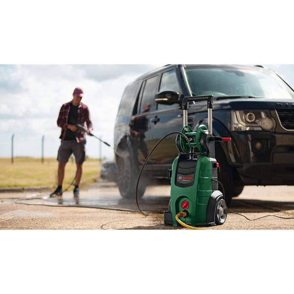 Bosch Hochdruckreiniger im Vordergrund, während eine Person im Hintergrund ein schwarzes Auto mit einer Spritzlanze reinigt.