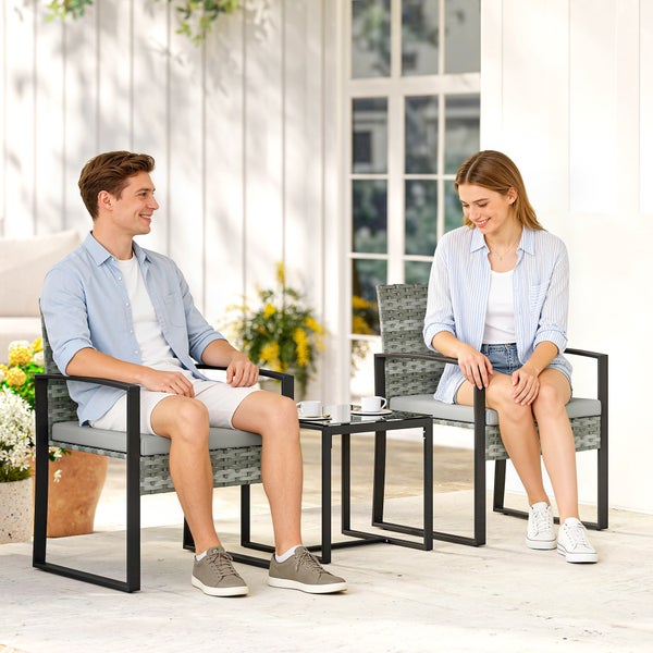 Zwei Personen sitzen auf grauen Gartenstühlen aus Polyrattan auf einer hellen Terrasse mit einem kleinen schwarzen Beistelltisch in der Mitte.