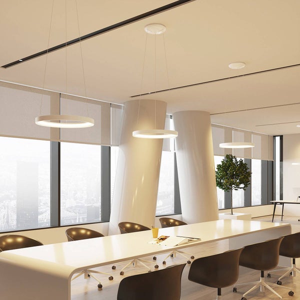 Heller, moderner Besprechungsraum mit drei ringförmigen LED-Pendelleuchten über einem weißen Konferenztisch und Fenstern mit Stadtblick.
