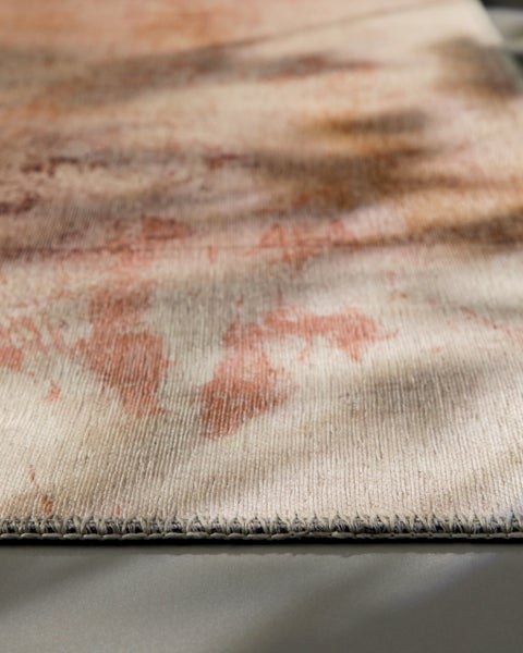 Detailaufnahme eines Teppichs mit abstraktem Muster in Braun und Beige sowie geketteltem Rand.