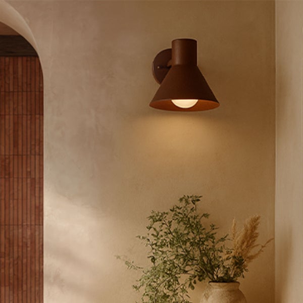 Wandleuchte mit kegelförmigem Schirm montiert an einer Wand über einer Vase mit Pflanzen.