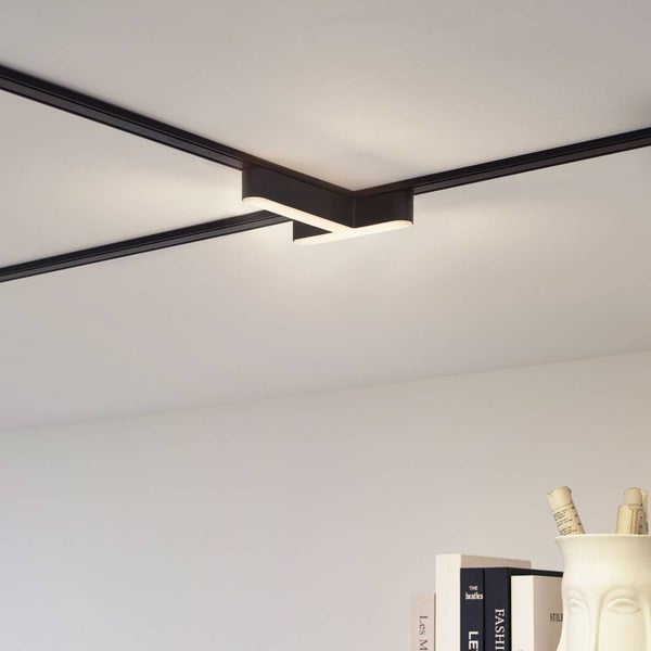 Modernes schwarzes Schienensystem an einer weißen Decke mit einem L-förmigen LED-Verbinder, der ein warmes Licht abgibt.