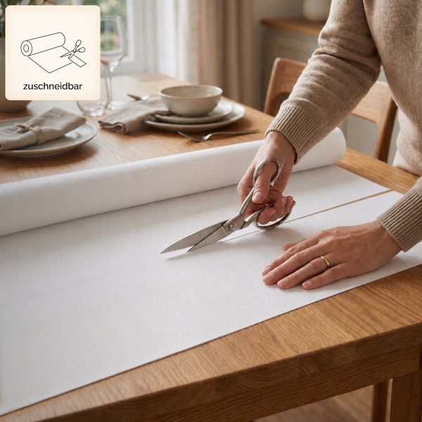Eine Person schneidet einen weißen Tischläufer mit einer Schere auf einem Holztisch zu. Symbol für individuell zuschneidbar.