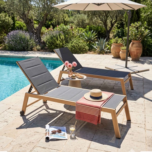 Zwei Gartenliegen aus Holz mit grauer Liegefläche am Pool unter einem Sonnenschirm auf einer Terrasse.