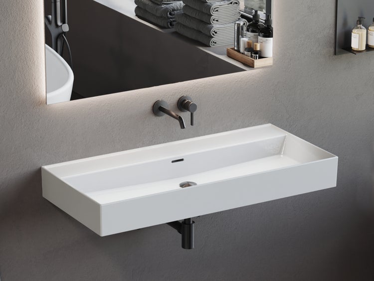 Rechteckiges Wand-Waschbecken aus weißer Keramik mit schwarzer Armatur, Siphon und beleuchtetem Spiegel in einem modernen Badezimmer.