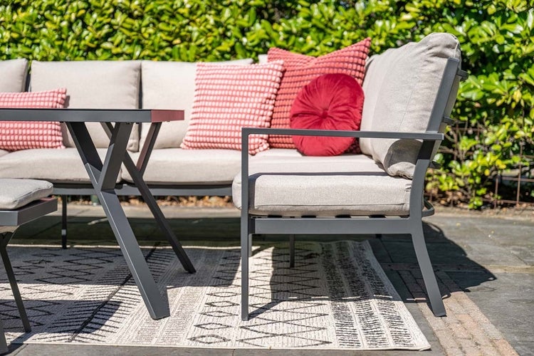 Modernes Garten-Lounge-Set aus Metall bestehend aus Ecksofa mit Polstern, Dekokissen, Beistelltisch und gemustertem Außenteppich auf einer Terrasse.