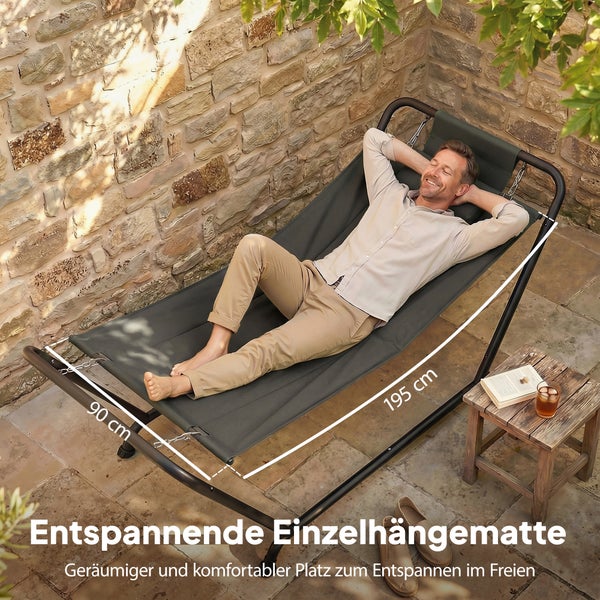 Helle Szene mit Mann in grauer Einzelhängematte auf Steinterrasse mit Mauerwerk und Holztisch. Maße 195 mal 90 Zentimeter.