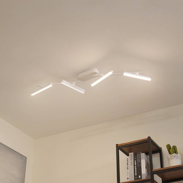 Moderne LED-Deckenleuchte mit vier verstellbaren Stablampen in Weiß, montiert an der Decke über einem Bücherregal in einem hellen Raum.