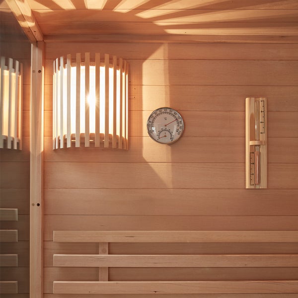 Saunainnenraum mit Holzwand, Saunalampe mit Holzblende, Thermometer und Sanduhr.