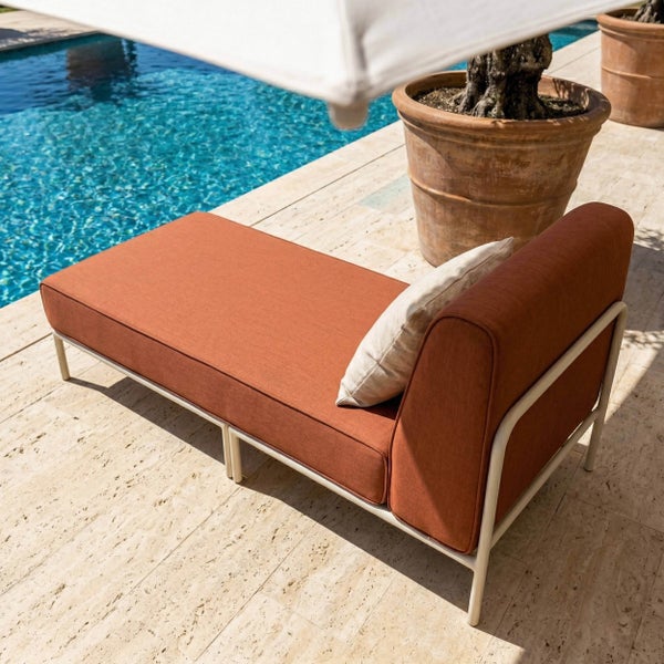 Moderne Sonnenliege mit terrakottafarbenem Polster und Metallgestell auf einer hellen Steinterrasse neben einem Pool.