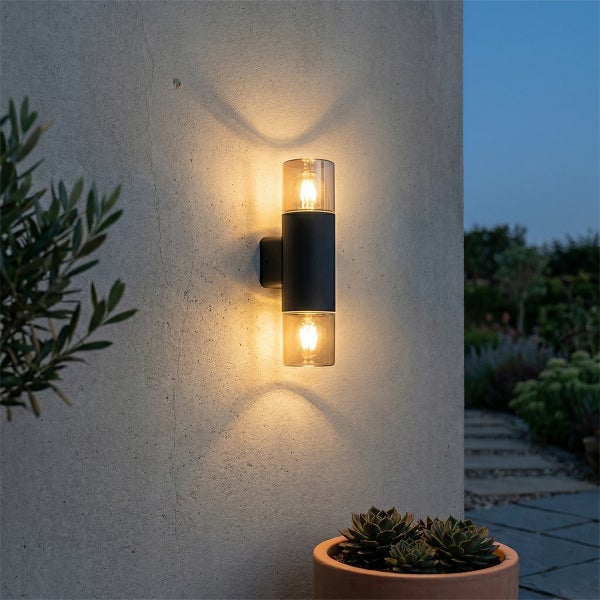Zylindrische Außenwandleuchte mit Up-and-Down-Licht an einer strukturierten Wand, die einen warmen, sanduhrförmigen Lichtschein erzeugt.
