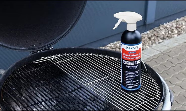 beko Backofen- und Grillreiniger Sprühflasche auf einem Grillrost in einem offenen Holzkohlegrill.