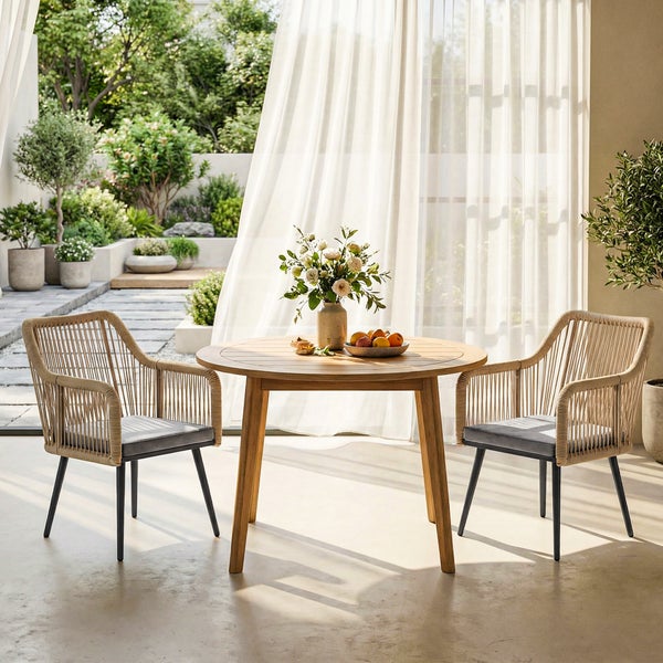 Modernes Gartenmöbel-Set mit rundem Holztisch und zwei Geflechtsesseln mit dunklen Sitzkissen auf einer hellen Terrasse vor einem Garten.