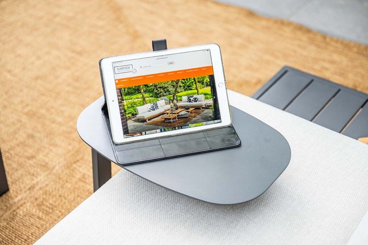 Tablet in einer Hülle auf einem kleinen Beistelltisch, der seitlich an einem Gartensofa montiert ist.