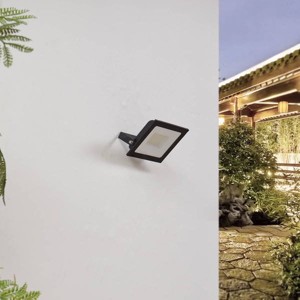 LED-Außenstrahler an einer Wand montiert, im Hintergrund ein beleuchteter Gartenweg mit Pflanzen und Holzpavillon.