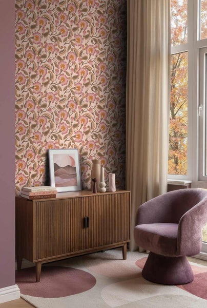 Wohnzimmer mit floral gemusterter Tapete, einem Holzsideboard, einem gepolsterten Sessel und einem Teppich vor einem Fenster.