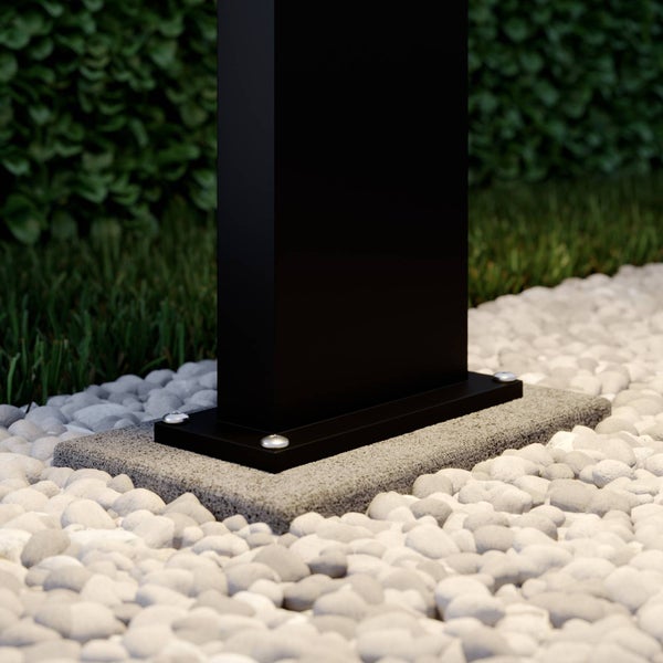 Schwarzer Pfosten auf einer grauen Bodenplatte verschraubt, umgeben von hellen Kieselsteinen im Garten.