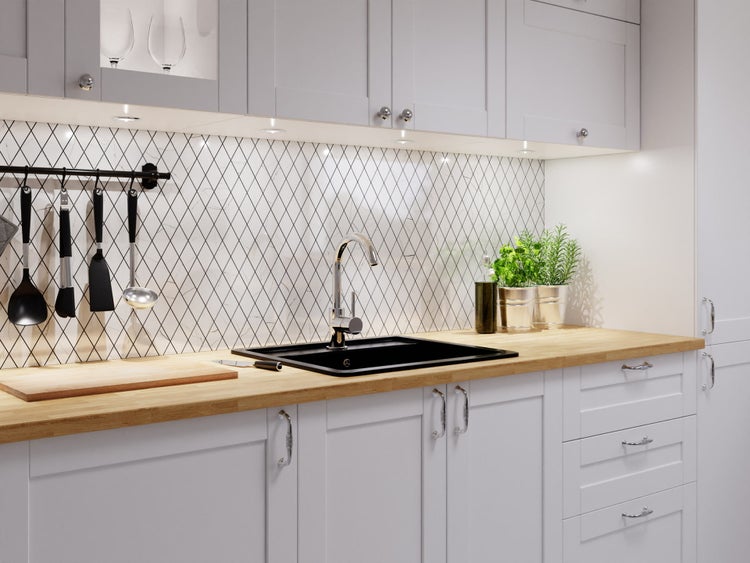 Helle Küche mit weißen Schränken, Holz-Arbeitsplatte, schwarzer Spüle und einem Fliesenspiegel mit Rautenmuster.