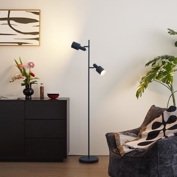 Moderne zweiflammige Stehleuchte aus Metall in Schwarz in einem Wohnzimmer mit Sideboard, Sessel und Zimmerpflanze.