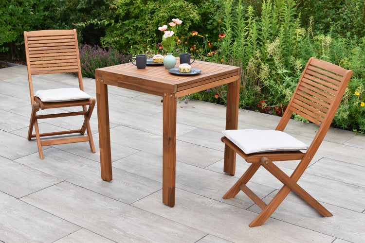 Quadratischer Holztisch mit zwei Holzklappstühlen und Sitzkissen im Garten.