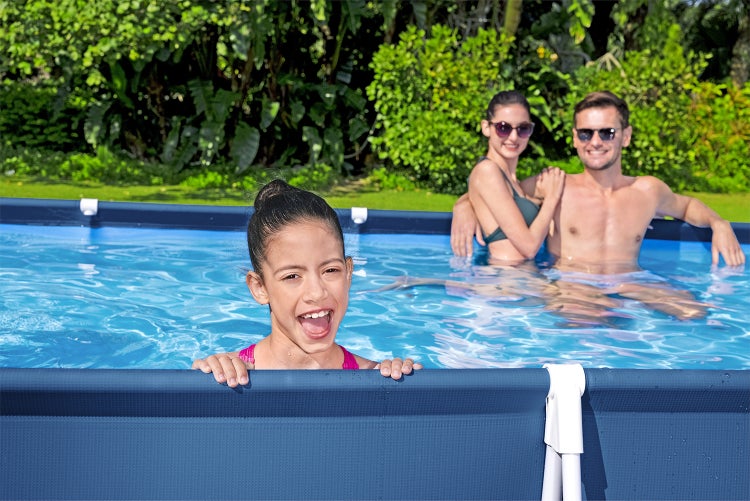 Familie in einem blauen rechteckigen Rahmenpool in einem hellen, grünen Garten.