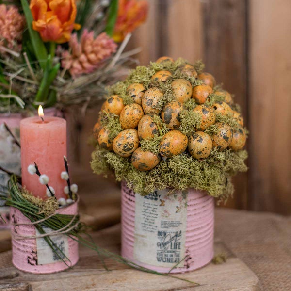 Dekorative Osterdekoration mit bemalten Eiern, Kerze und Blumen in Dosen