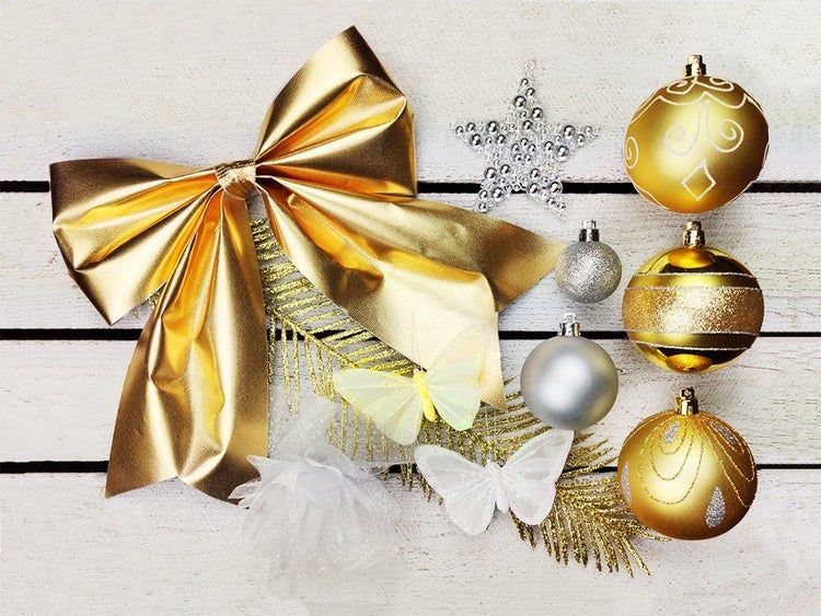 Set aus Weihnachtsschmuck bestehend aus einer Schleife, Weihnachtskugeln, Dekosternen und Schmetterlingen auf einer Holzoberfläche.