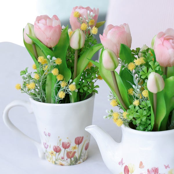 Kunstblumen-Arrangement mit rosa Tulpen in einer weißen Tasse und Kanne mit floralem Dekor.
