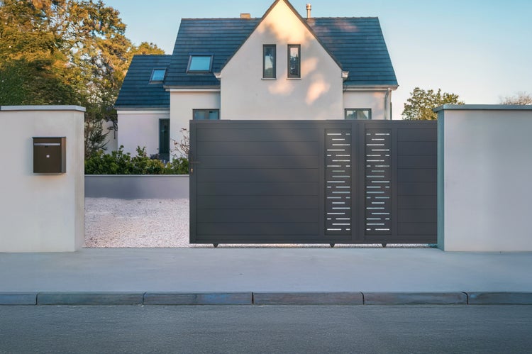 Modernes Schiebetor in Anthrazit mit horizontalen Lamellen und dekorativen Aussparungen an einer Grundstückseinfahrt vor einem Wohnhaus.