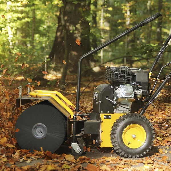 Eine benzinbetriebene Kehrmaschine mit rotierender Bürste entfernt Laub auf einem Waldweg.