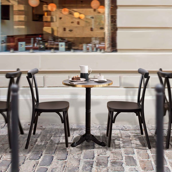 Outdoor-Bistro-Set mit rundem schwarzem Tisch mit goldfarbenem Rand und zwei schwarzen Holzstühlen auf Kopfsteinpflaster vor einem Café.