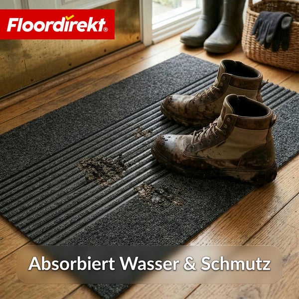 Floordirekt Logo. Schmutzfangmatte mit Rillenstruktur im Eingangsbereich auf Holzfußboden mit schmutzigen Arbeitsschuhen.