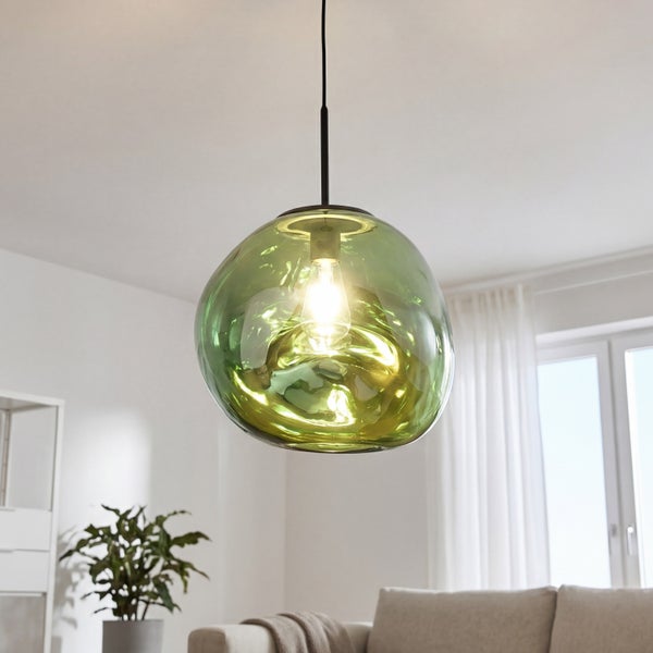 Pendelleuchte mit organisch geformtem grünem Glasschirm in einem hellen Wohnzimmer mit Sofa und Zimmerpflanze.