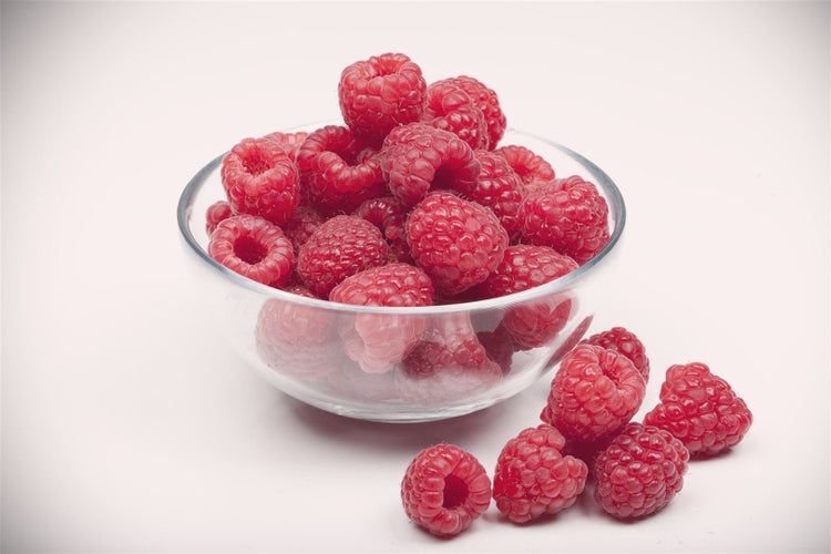 Eine Glasschale gefüllt mit frischen Himbeeren auf weißem Untergrund.