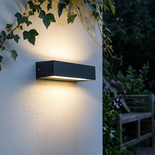 Moderne rechteckige Außenwandleuchte mit direktem und indirektem Licht an einer Hauswand im Außenbereich.