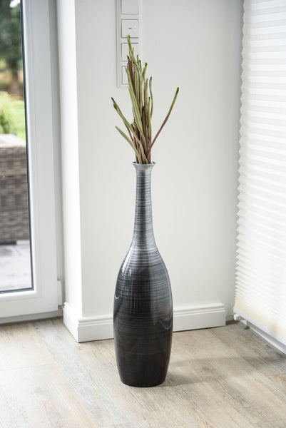 Hohe, dekorative Bodenvase mit strukturierter Oberfläche und Zweigen in einem hellen Raum.