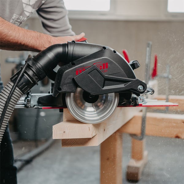 Handwerker beim Einsatz einer Mafell Tauchsäge mit angeschlossenem Absaugschlauch zum Sägen eines Holzbalkens in einer Werkstatt.