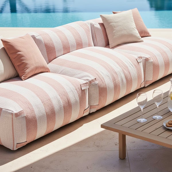 Modernes Outdoor Lounge Sofa mit weiß lachsfarbenen Streifen und passenden Kissen auf einer hellen Terrasse am Pool mit einem Holz Couchtisch.